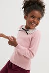 Young girl wearing the classic Dusty Pink Blanca Merino Wool Girl Jumper with lace collar and black bow, embodying effortless, high-end style and fun sophistication.