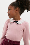 Young girl in a classic, dusty pink Blanca Merino Wool Girl Jumper with lace collar and velvet bow, embodying effortless, high-end style and playful elegance.