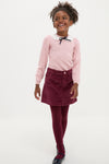 Young girl wearing the classic Dusty Pink Blanca Merino Wool Girl Jumper with lace collar and black bow, paired effortlessly with a wine-colored corduroy skirt and burgundy tights.
