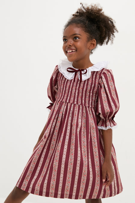 Young girl in a classic Burgundy Floral Stripe Festa Girl Hand-Smocked Dress, featuring an effortless fit-and-flare silhouette, lace trims, and a charming Peter Pan collar.