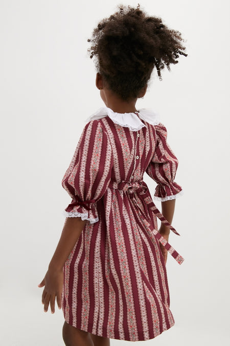 Child in classic Burgundy Floral Stripe Festa Dress, featuring an effortless fit-and-flare silhouette with a Peter Pan collar, lace trims, and a charming bow detail.