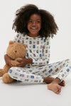 Young girl in the Ballet Slippers Kids Bamboo Pj Set, featuring an ice skate pattern, hugging a teddy bear. The classic, effortless pajama set is both fun and high-end.