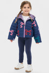 Young girl wearing the classic, effortless Girls Reversible Riley Jacket with bright bow motifs, perfect for fun, high-end style and versatile, weather-resistant outings.