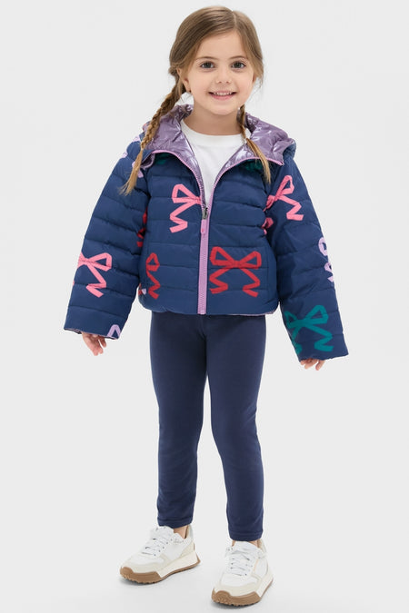 Young girl wearing the classic, effortless Girls Reversible Riley Jacket with bright bow motifs, perfect for fun, high-end style and versatile, weather-resistant outings.