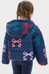 Young girl in a classic, fun, navy-blue Girls Reversible Riley Jacket with colorful bows, embodying effortless style and high-end versatility against a light background.