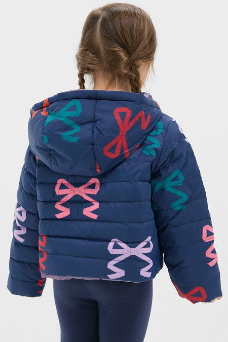 Young girl in a classic, fun, navy-blue Girls Reversible Riley Jacket with colorful bows, embodying effortless style and high-end versatility against a light background.