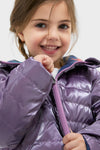 Young girl beams while zipping the Girls Reversible Riley Jacket, showcasing its classic, fun, and effortless high-end design with a metallic purple side.