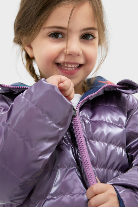 Young girl beams while zipping the Girls Reversible Riley Jacket, showcasing its classic, fun, and effortless high-end design with a metallic purple side.