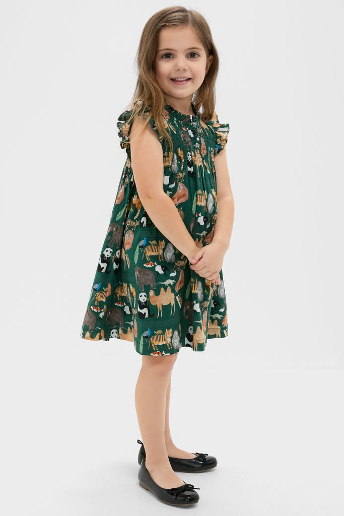 Young girl wearing the classic and high-end Girls Stevie Dress, featuring effortless smocked bodice, fun animal print, flutter sleeves, and ballet flats.