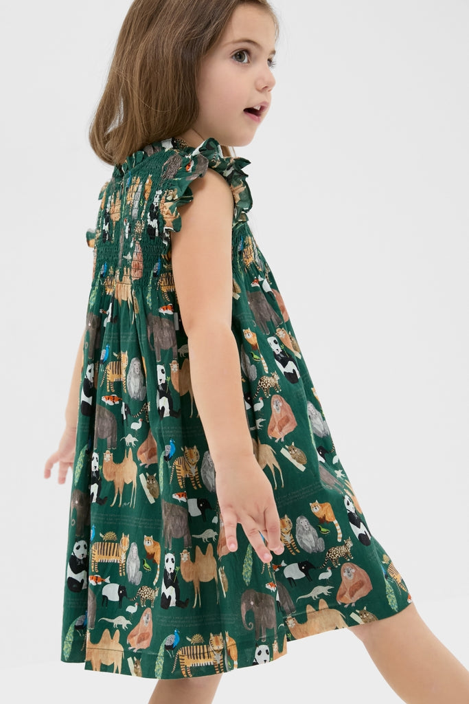 Young girl in a classic, fun Girls Stevie Dress, featuring a sleeveless, forest-green animal print with effortless ruffle details and high-end smocked bodice, embodying Tuckernuck's cool style.