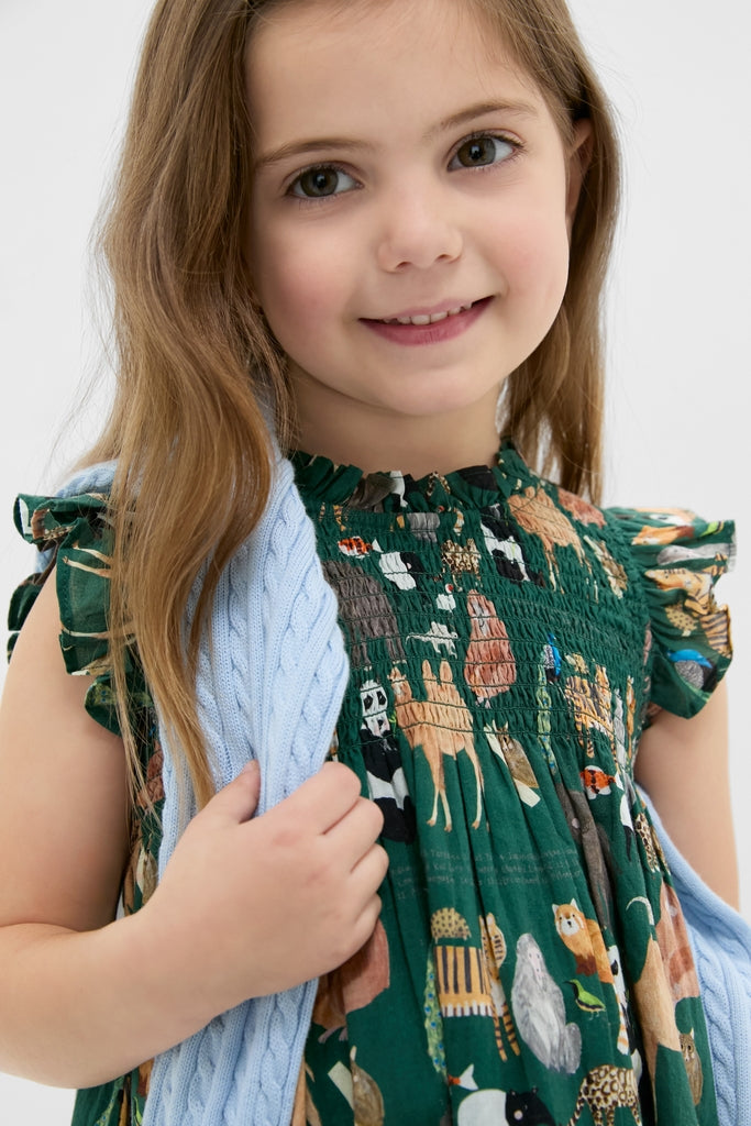 Young girl smiling in a classic, effortless Girls Stevie Dress with animal print, paired with a fun cable-knit sweater, showcasing high-end, playful style.