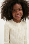 Young girl smiles, wearing Polo Ralph Lauren's Girls Long-Sleeve Cotton Cable Knit Lurex Cardigan, showcasing a classic, high-end, and effortlessly stylish design with button placket and ribbed hems.