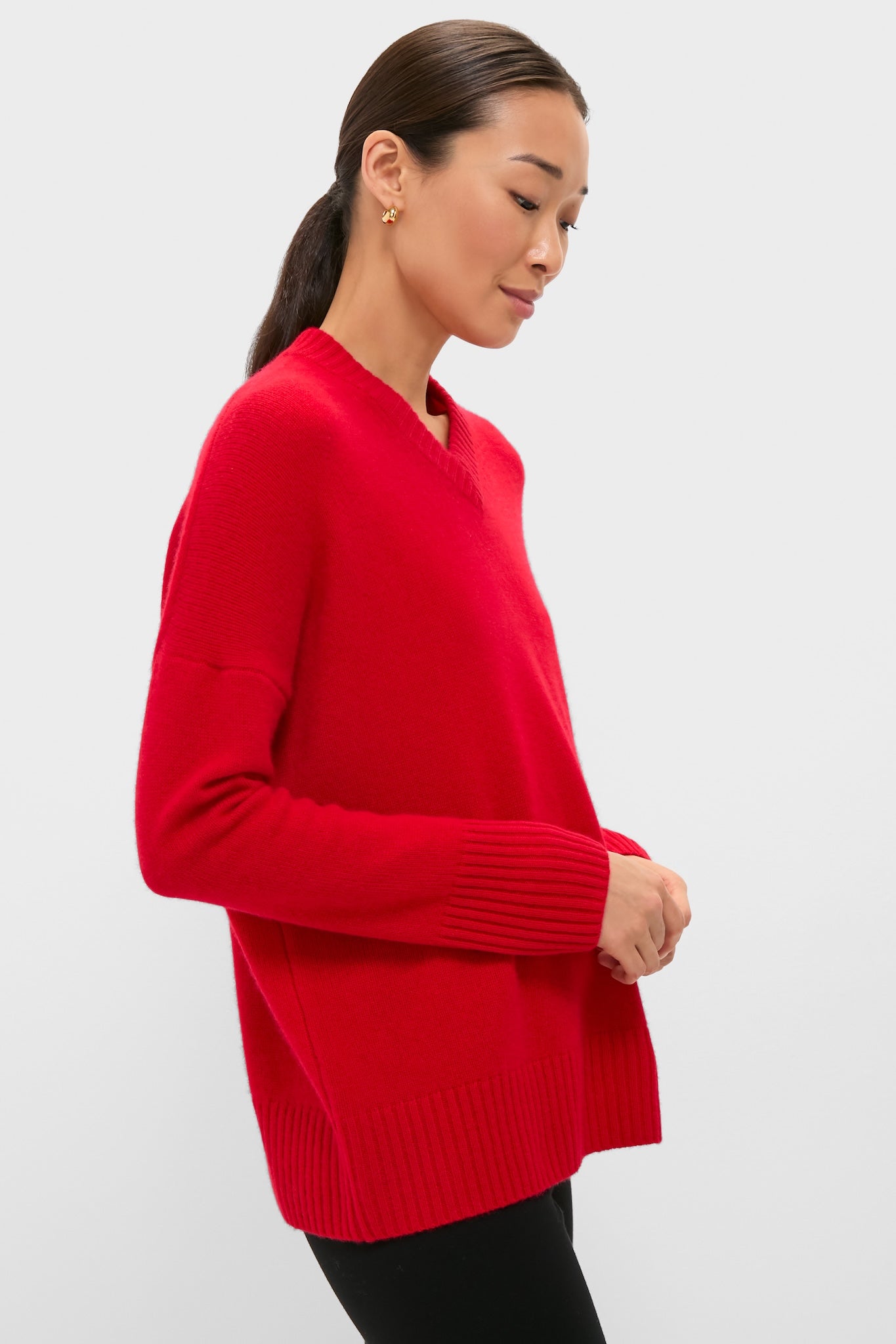 Woman in profile wearing Martin Red Cashmere Cassie V-Neck Sweater with ribbed cuffs, embodying classic, effortless style. Perfect blend of fun and high-end fashion.