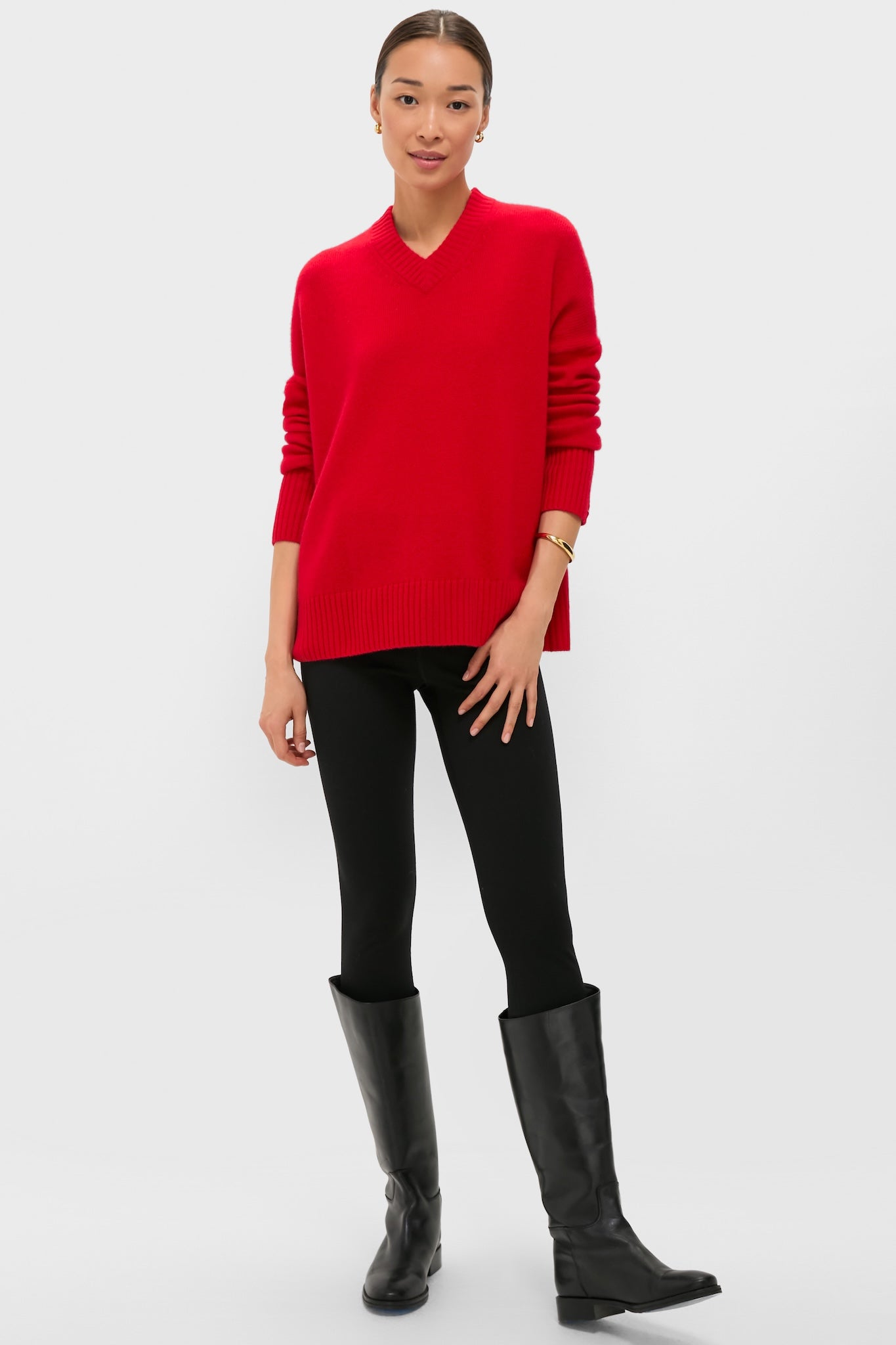 Woman models the classic Martin Red Cashmere Cassie V-Neck Sweater, featuring a relaxed fit and ribbed finishes, paired effortlessly with black leggings and boots.