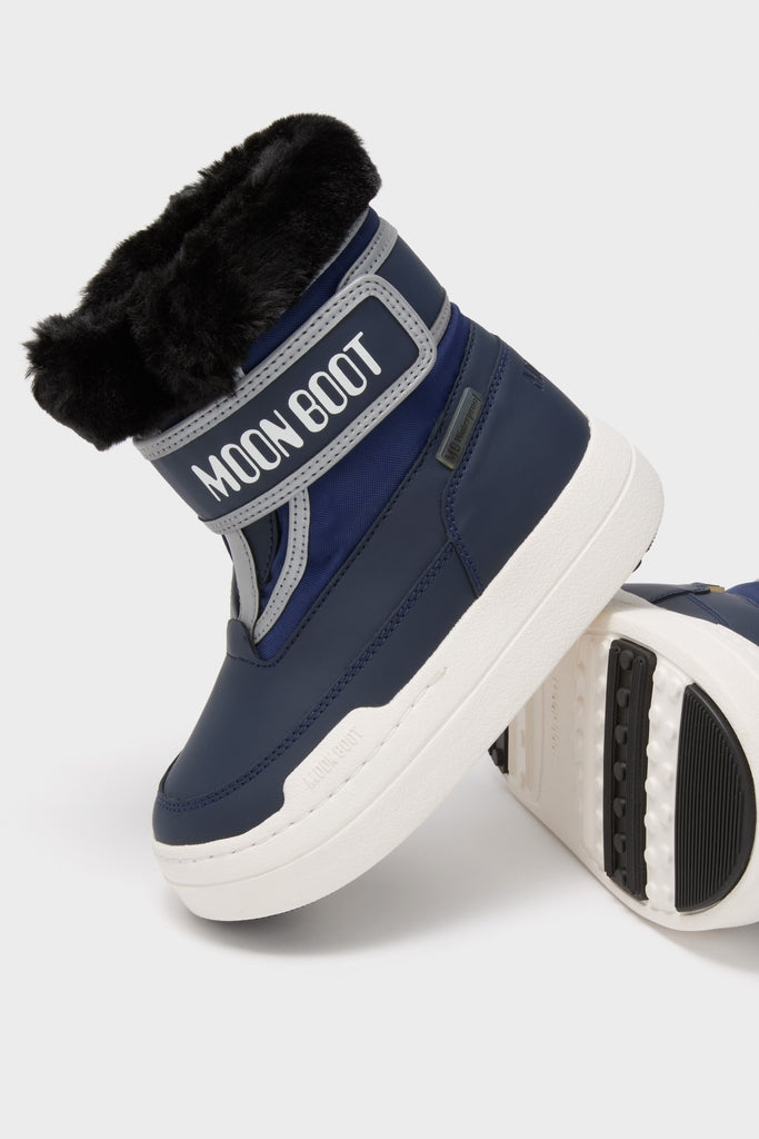 Kids Navy Jr Parkstrap Boots, featuring a classic Moon Boot design with a chunky white sole, faux-fur cuff, and velcro strap, offer an effortless, fun, high-end winter style.