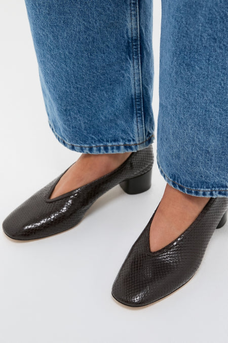 Classic, effortless style: Printed Python Luna Pumps in black leather, featuring a low block heel and V-shaped topline, paired with cropped denim jeans for a fun, high-end look.