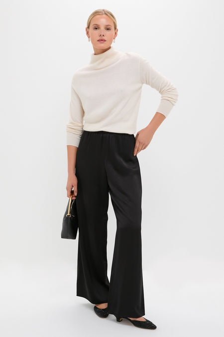 Woman wearing classic turtleneck and wide-leg pants, holding a high-end handbag, with effortless Black Crystals Erika Pump Sandals adding a fun, textured sparkle to her look.
