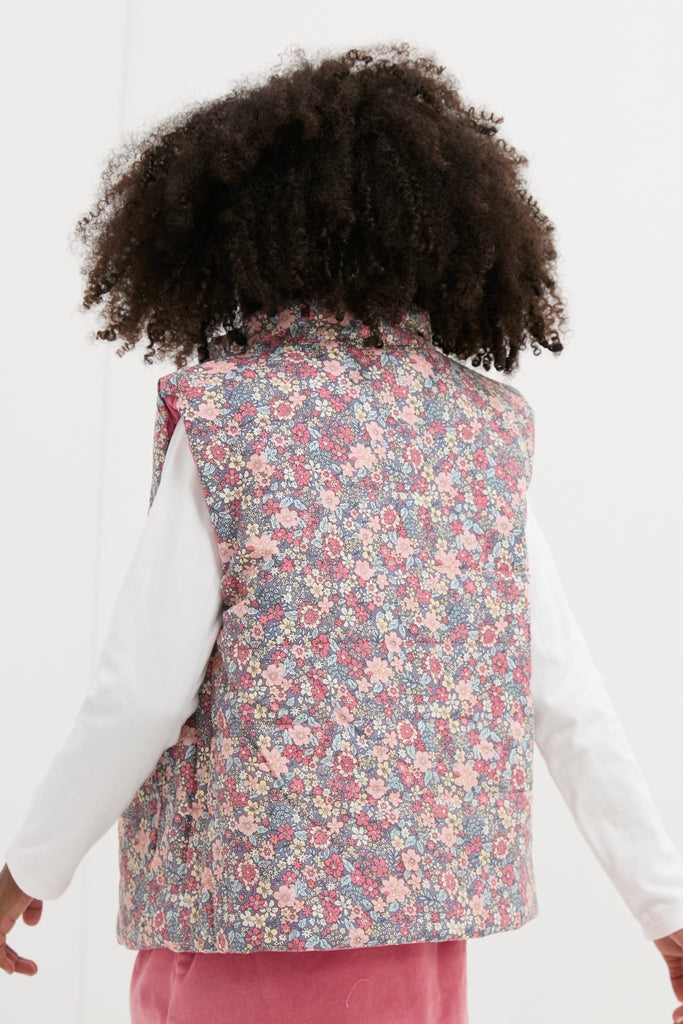 Person in a classic, reversible Floral Padded Gilet, effortlessly styled over a white shirt, embodying a high-end, fun aesthetic. Ideal for confident, everyday adventures.