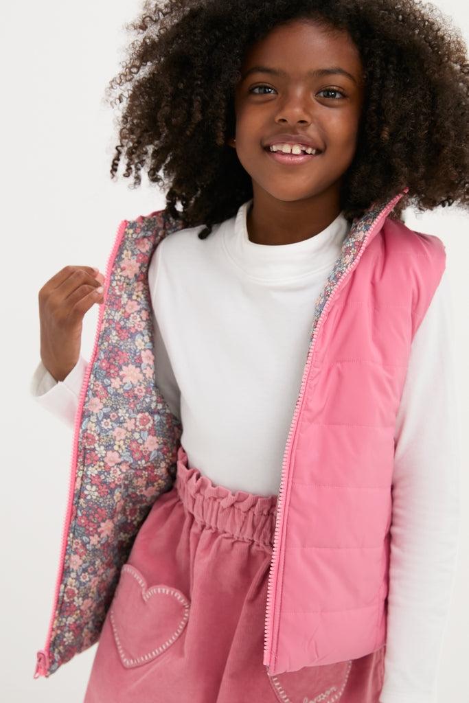 Young girl in a classic, fun pink Padded Gilet with a floral lining, showcasing effortless style and high-end craftsmanship through its reversible design and heart-shaped pocket details.