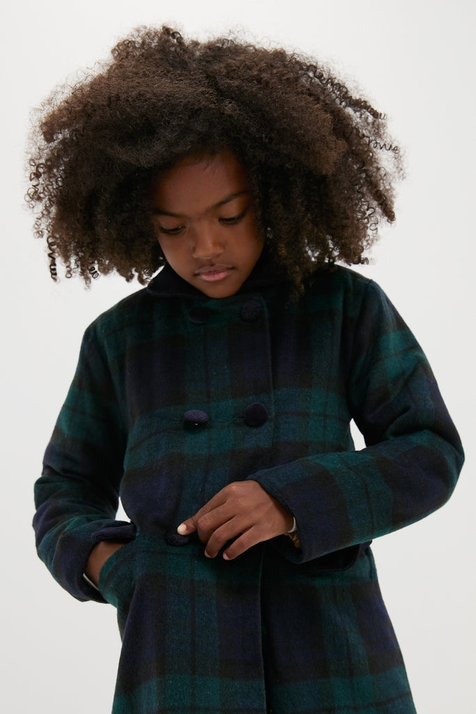 Child in a classic Blackwatch Velvet Trim Coat with a green and navy tartan pattern, fastening a button, showcasing effortless style with luxurious velvet details, ideal for any occasion.
