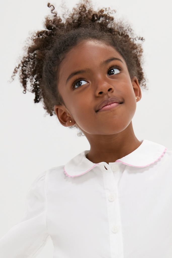 Young girl in a Ric Rac Blouse with scalloped collar and pink trim, exuding classic charm and effortless style, embodying Tuckernuck's fun, high-end fashion ethos.
