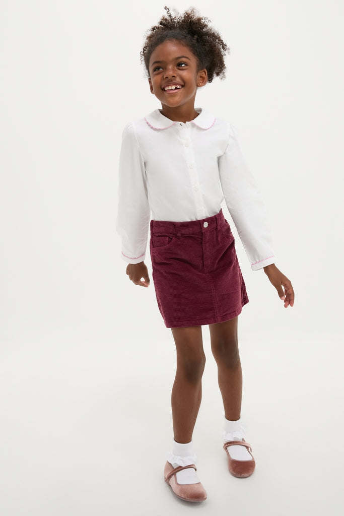 Young girl wearing the classic Ric Rac Blouse with pink trim, effortlessly paired with a burgundy skirt, embodying fun and high-end style.