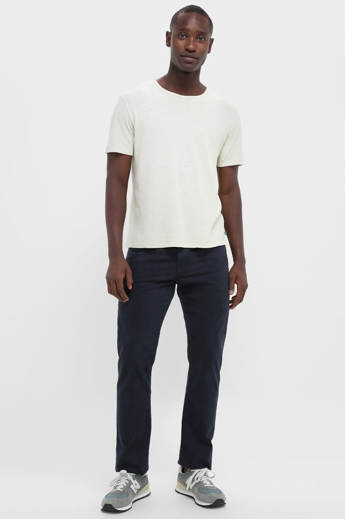 Man in an off-white Sand Drift Linen Tee, navy trousers, and gray sneakers, embodying classic, effortless style. Perfect for a fun, high-end summer look.