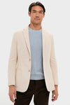 Man wearing the classic Tan Knit Travel Blazer by Tuckernuck, styled with a pale blue sweater and brown trousers, embodying effortless, high-end travel readiness.