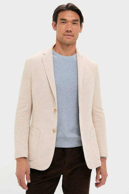 Man wearing the classic Tan Knit Travel Blazer by Tuckernuck, styled with a pale blue sweater and brown trousers, embodying effortless, high-end travel readiness.