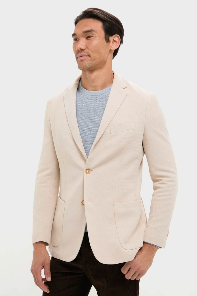 Man wearing Tan Knit Travel Blazer, effortlessly styled with a light blue crewneck and dark trousers, embodying classic and high-end travel-ready fashion for fun, confident journeys.