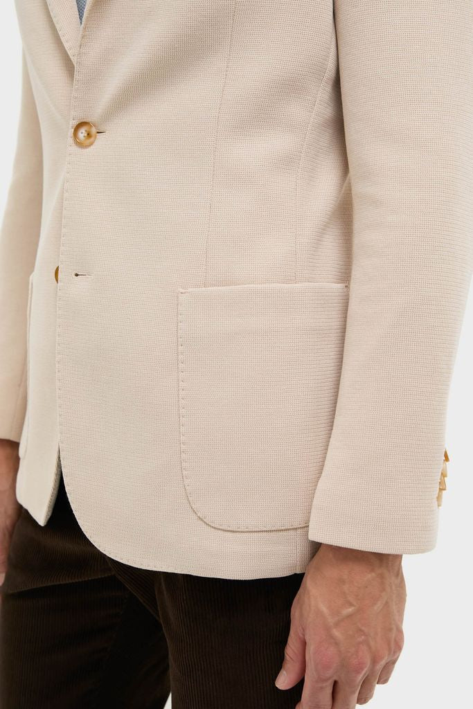 Close-up of a Tan Knit Travel Blazer on a person, showcasing its classic, effortless design with textured fabric, patch pocket, and button detail.
