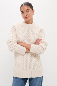 Young woman wearing the Ivory Galway Fisherman Sweater, a classic cable-knit with ribbed finishes, paired with blue jeans, embodying effortless, high-end style.