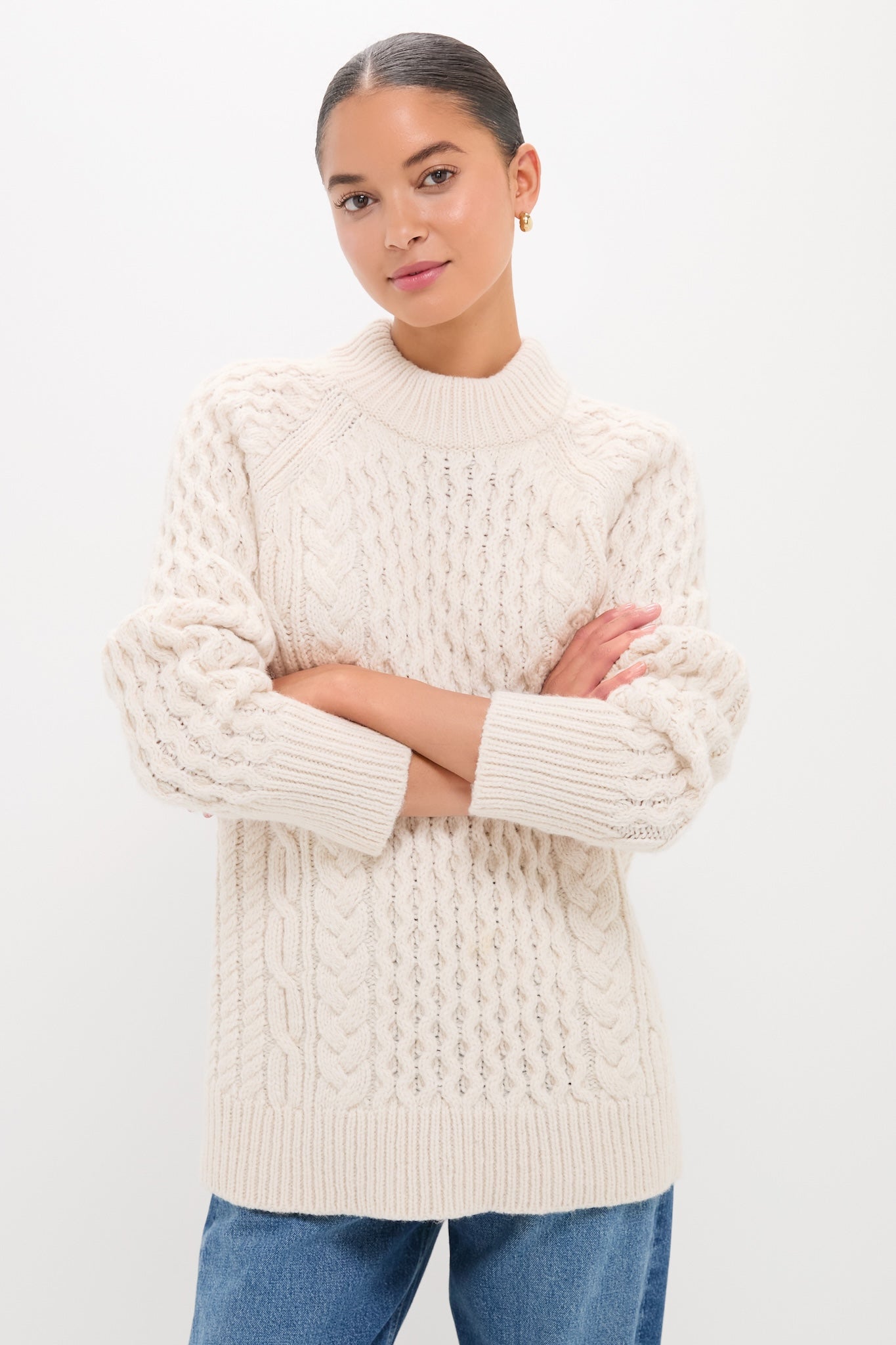 Woman in Ivory Galway Fisherman Sweater with cable-knit texture and relaxed fit, showcasing classic style and effortless warmth. Perfectly paired with medium-wash jeans for a fun, high-end look.
