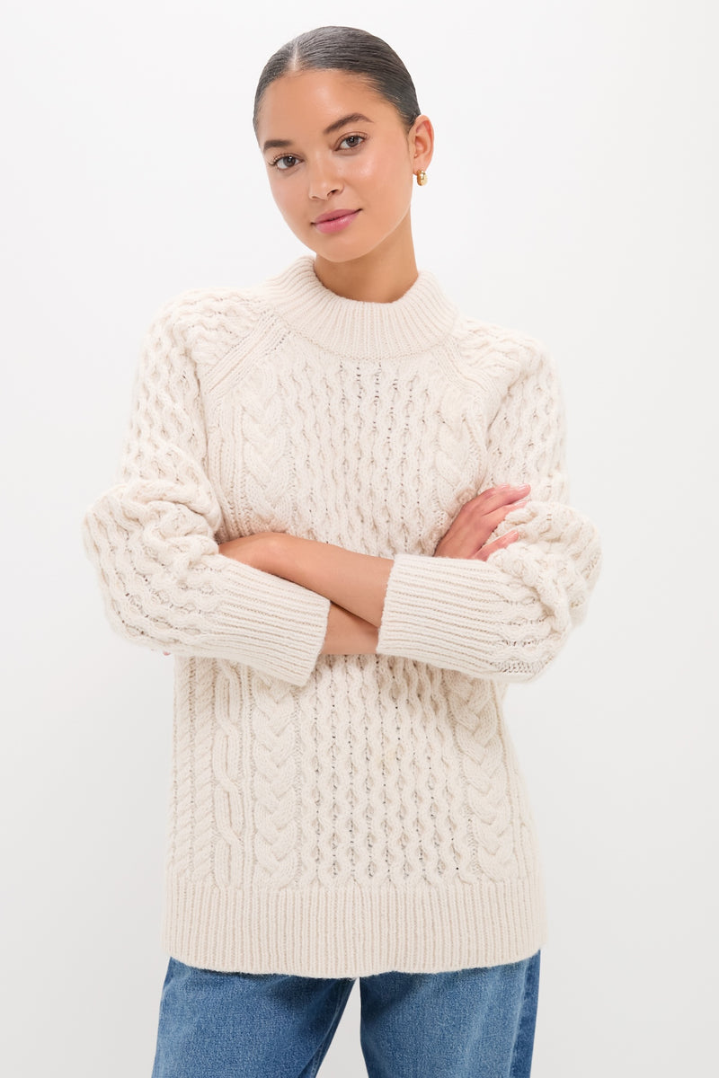 Woman in Ivory Galway Fisherman Sweater with cable-knit texture and relaxed fit, showcasing classic style and effortless warmth. Perfectly paired with medium-wash jeans for a fun, high-end look.