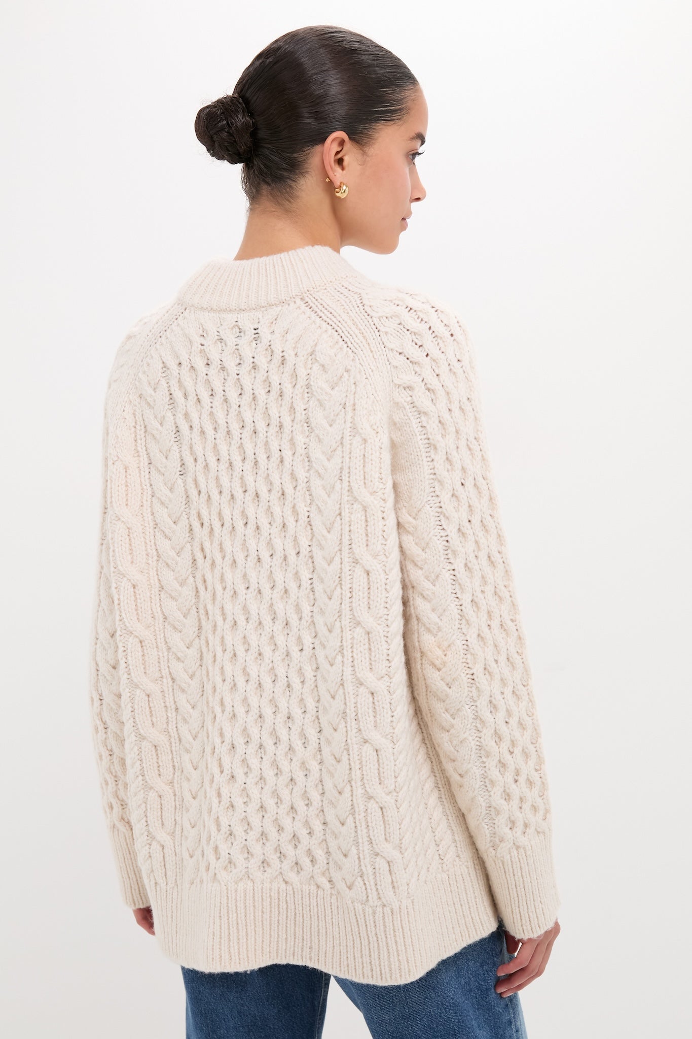 Model wearing the Ivory Galway Fisherman Sweater, showcasing its classic cable-knit texture and relaxed fit, paired effortlessly with jeans for a high-end, fun look.
