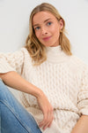 Ivory Galway Fisherman Sweater on young woman, showcasing classic cable-knit design and relaxed fit for effortless, high-end style. Perfectly paired with light blue jeans for timeless, fun fashion.