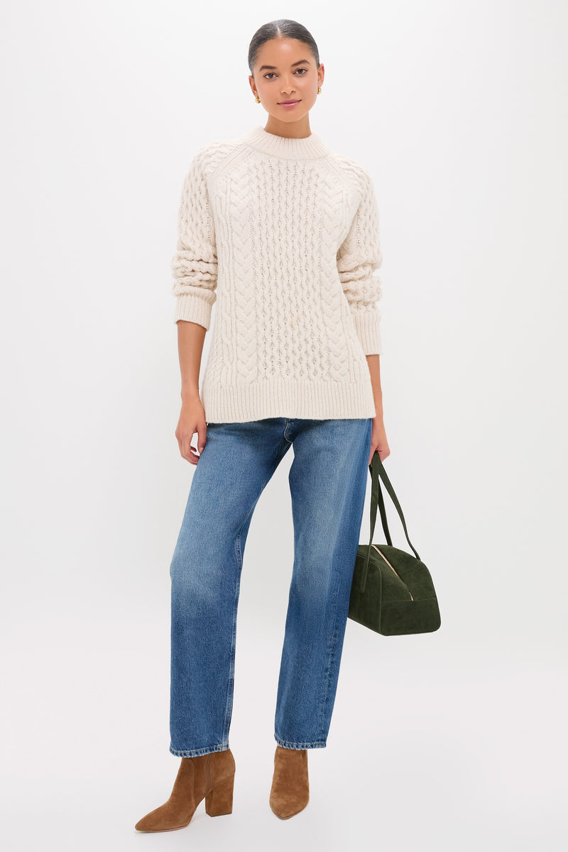 Model in Ivory Galway Fisherman Sweater, showcasing classic cable-knit with a relaxed fit, styled effortlessly with jeans, tan boots, and a chic green handbag.