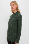 Young woman models the Hunter Green Galway Fisherman Sweater, showcasing its classic cable-knit design, relaxed fit, and ribbed crewneck for an effortless, high-end style.