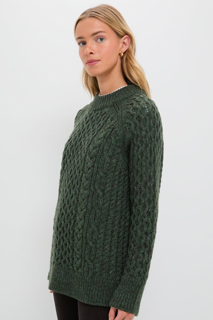 Young woman models the Hunter Green Galway Fisherman Sweater, showcasing its classic cable-knit design, relaxed fit, and ribbed crewneck for an effortless, high-end style.