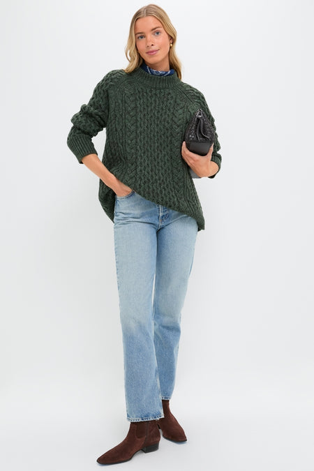 Model wearing the Hunter Green Galway Fisherman Sweater, a classic, oversized cable-knit with ribbed trim, styled effortlessly with jeans and a quilted handbag for a high-end, fun look.