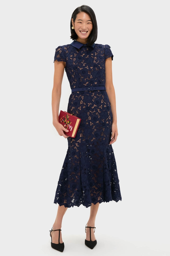 Model in navy lace dress holds the Camelia Holly Jingle and Mingle Book Clutch, a classic, high-end, hand-embroidered accessory for an effortless, fun style.