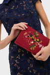 Person holds the classic Camelia Holly Jingle and Mingle Book Clutch, featuring festive embroidery, embodying high-end, effortless style and fun for book lovers.