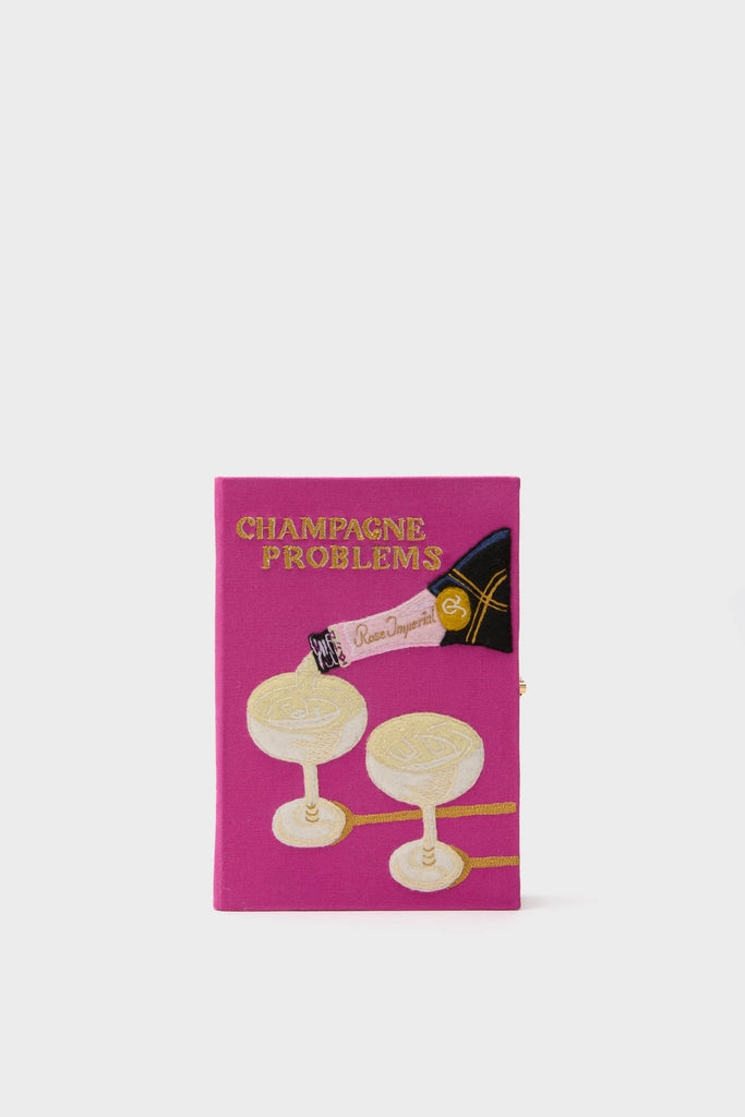 Fuchsia Champagne Problems Book Clutch, a classic hot-pink purse resembling a book with gold embroidery, effortlessly blending whimsy and high-end style for book lovers and fashionistas.