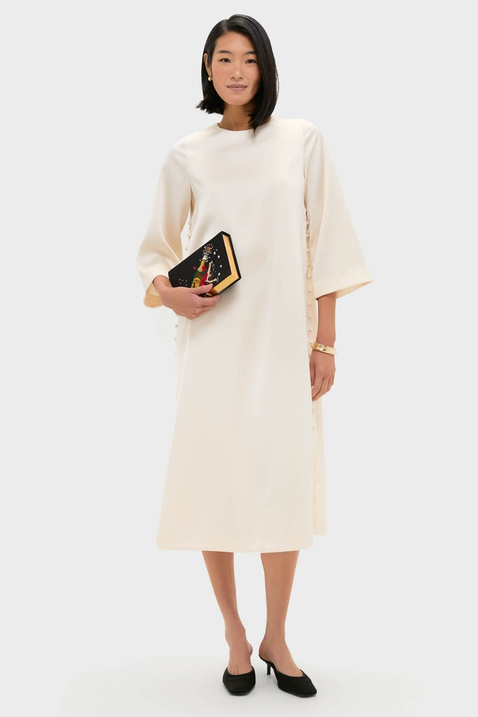 Woman models an ivory dress, showcasing the Black Starry Night Spectacular Book Clutch—a classic, high-end, hand-embroidered accessory, perfect for an effortless, fun, and stylish look.