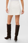 Model in Cream Wool Meg Mini Skirt, showcasing a classic, effortless style with an A-line shape, paired with dark brown suede knee-high boots for a fun, high-end look.