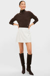 Woman in a classic, effortless Cream Wool Meg Mini Skirt, styled with a fitted turtleneck and knee-high boots, embodying high-end, fun fashion.