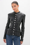 Model wearing the Black Vegan Leather Military Jacket with a high collar, silver snap-buttons, and princess seams, paired with blue jeans for a classic, effortless, high-end look.