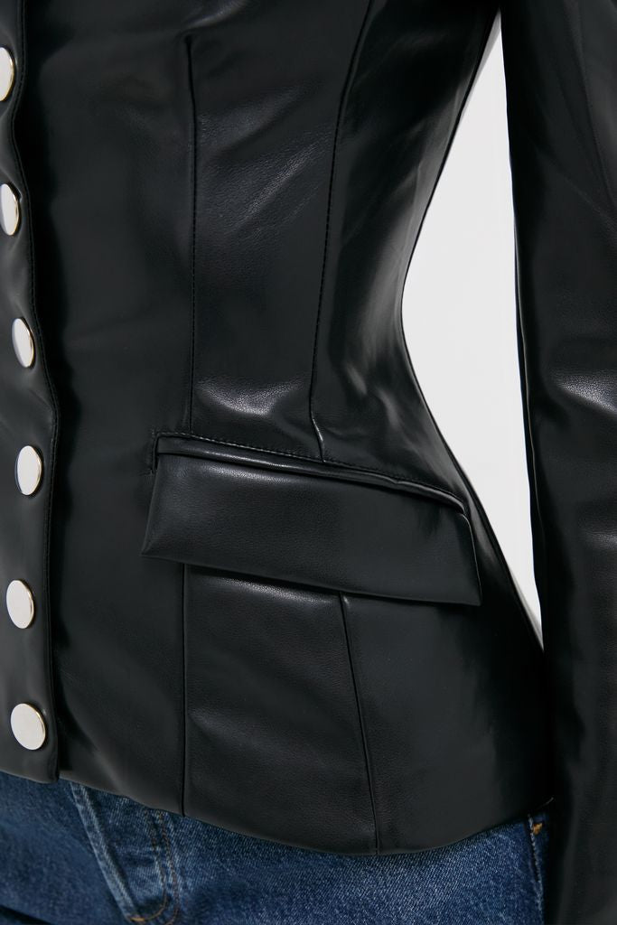 Black Vegan Leather Military Jacket with classic silver buttons and a flap pocket, effortlessly styled over blue jeans, exuding a fun, high-end vibe.