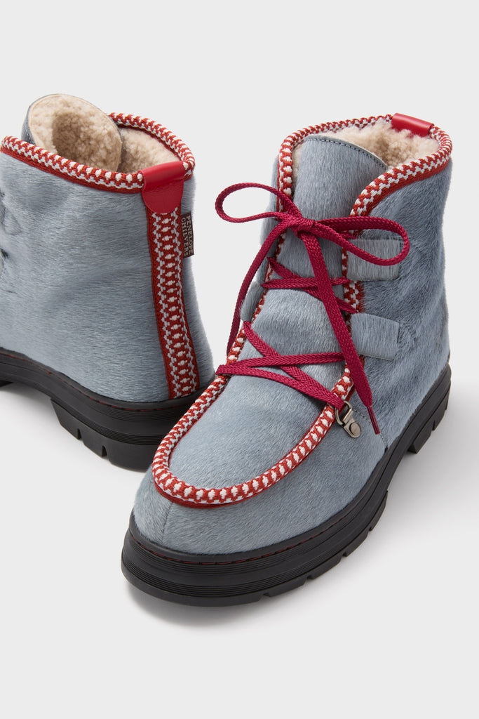 Mist Incredible Pony Shearling-Lined Boots, featuring a bluish-gray pony-hair finish, red braided trim, and chunky black soles, offer a classic, effortless, and fun high-end winter style.