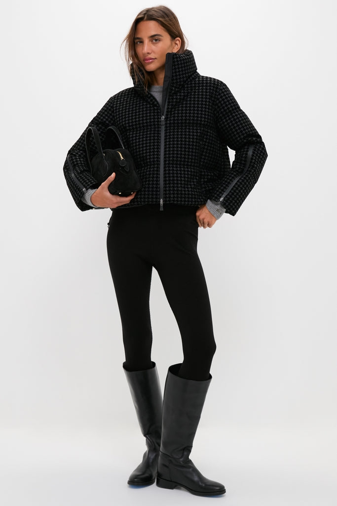 Woman models the Black Tech Pied de Poule Short Jacket, a high-end, classic puffer with houndstooth pattern and feather padding, styled effortlessly with black leggings and boots.